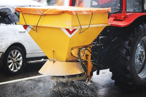 Tractor with mounted salt spreader, road maintenance - winter gritter vehicle.  Tractor de-icing street, spreading salt. Municipal service melting ice on streets in winter. Diffuser of salt blend on road